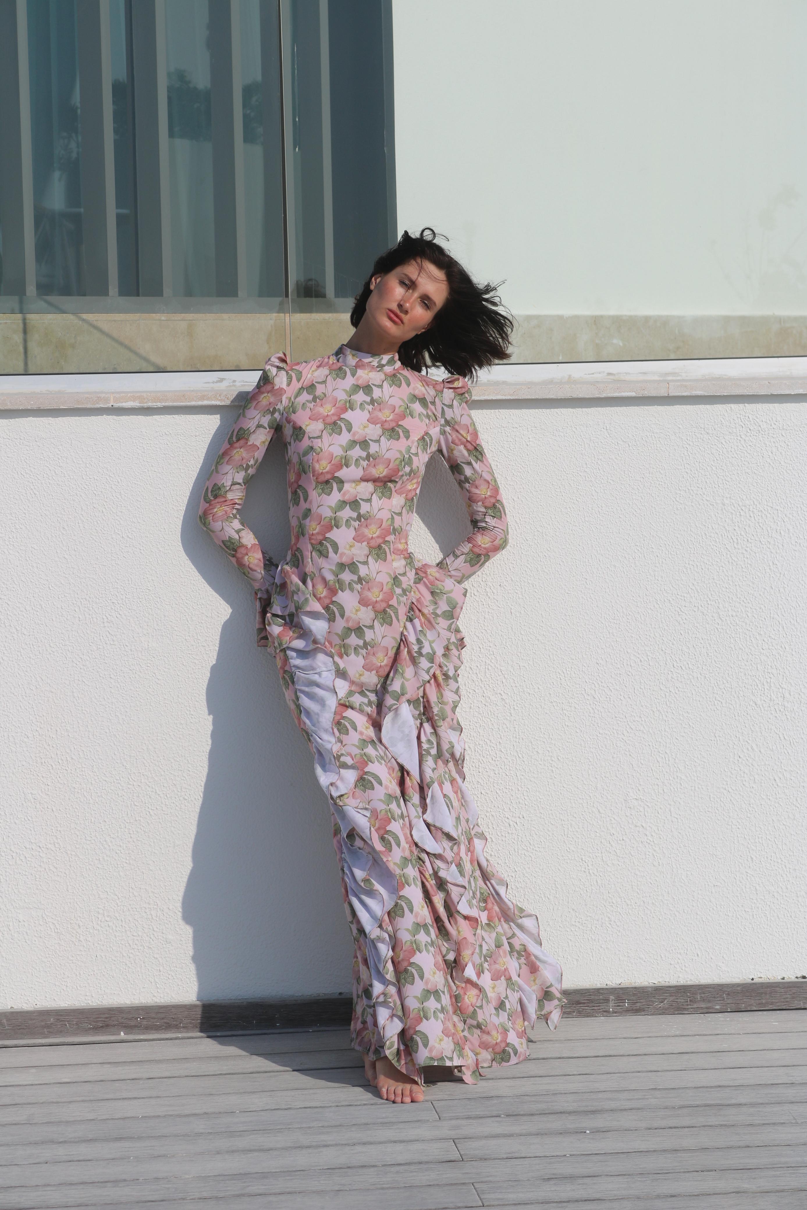 Woman in a floral dress standing on a rooftop with a building in the background